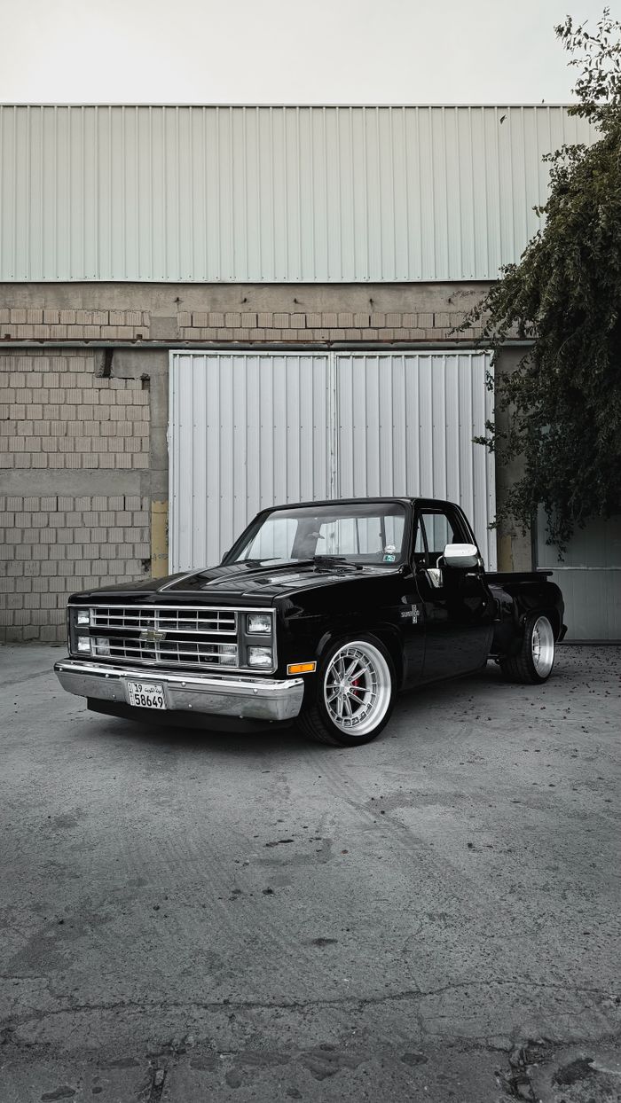 services-02 A classic black Chevrolet pickup truck parked in an urban area with a warehouse backdrop.