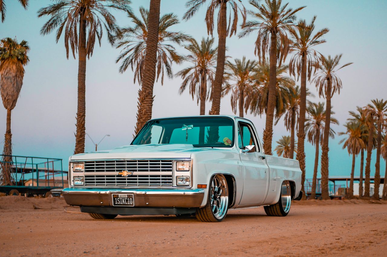 gallery-3 Vintage pickup truck parked under palm trees during a vibrant sunset, creating a nostalgic and warm atmosphere.