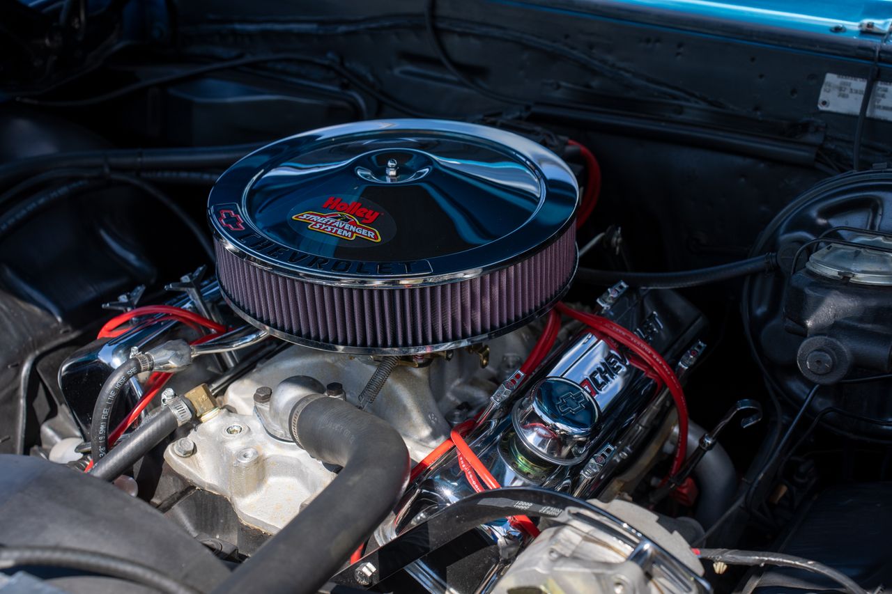 services-01 Detailed view of a classic car engine featuring a shiny Holley air filter and red ignition wires.